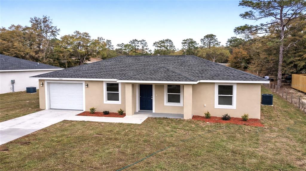 A single-story house with a tan stucco exterior, a dark blue door, and a gray roof — 15350 SW 38TH PLACE, OCALA, FL