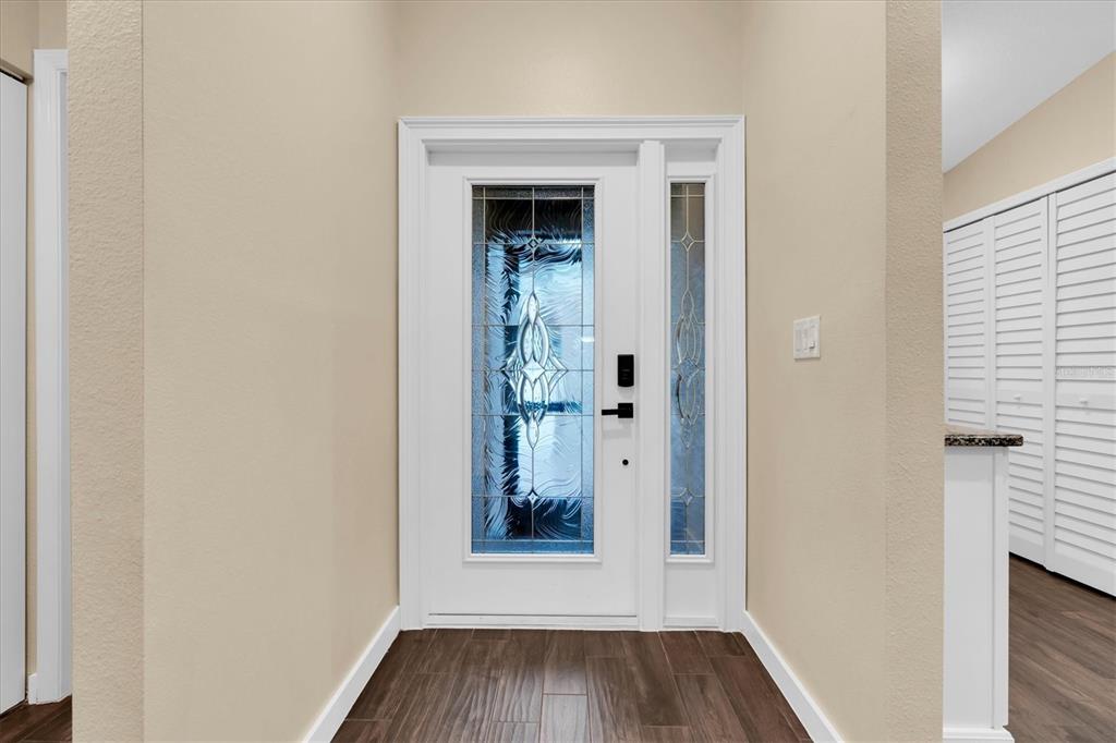A white front door with decorative glass panels sits in a foyer with wood-look flooring — 3203 CHARTER CLUB DRIVE UNIT B, TARPON SPRINGS, FL