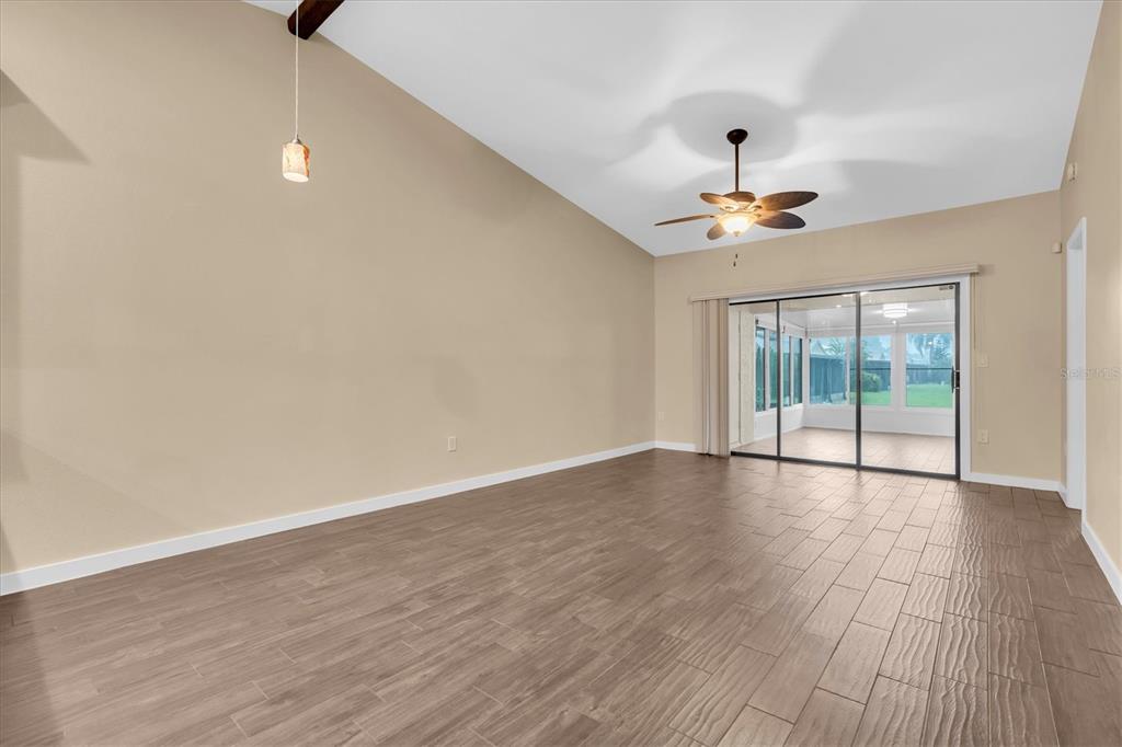 A spacious living room features vaulted ceilings, wood-look tile flooring, and sliding glass patio doors — 3203 CHARTER CLUB DRIVE UNIT B, TARPON SPRINGS, FL