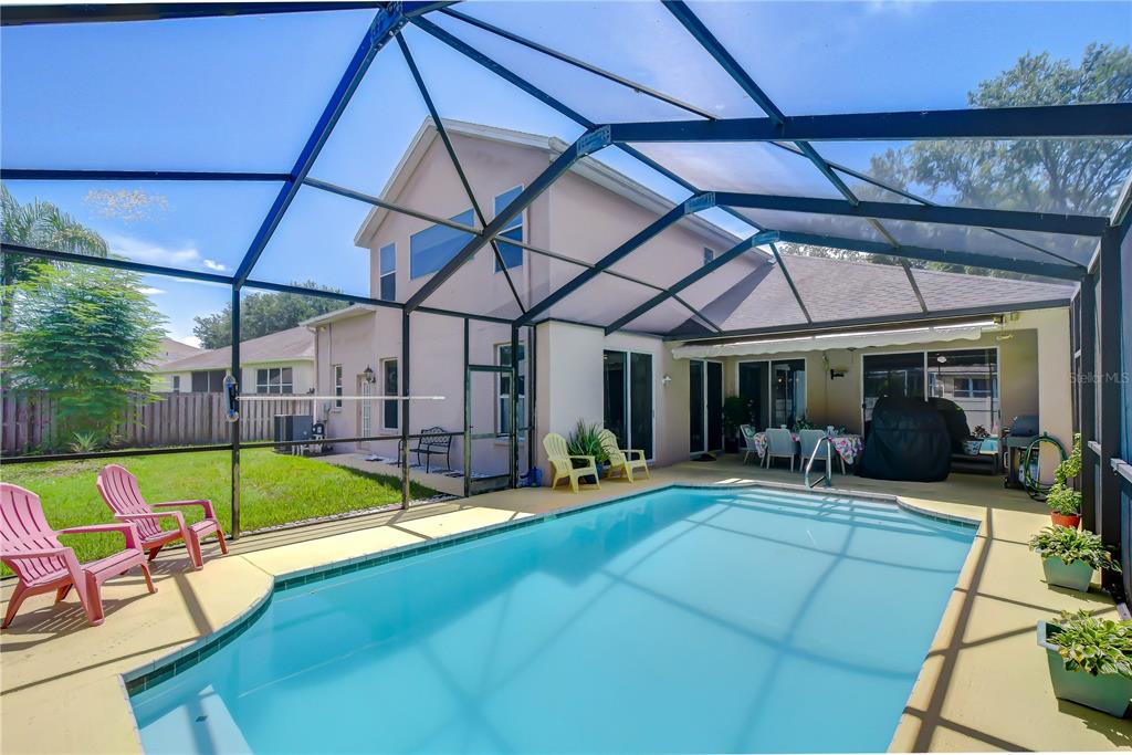 A swimming pool with a screened enclosure sits behind a two-story house with a lawn — 2202 LONGMORE CIRCLE, VALRICO, FL