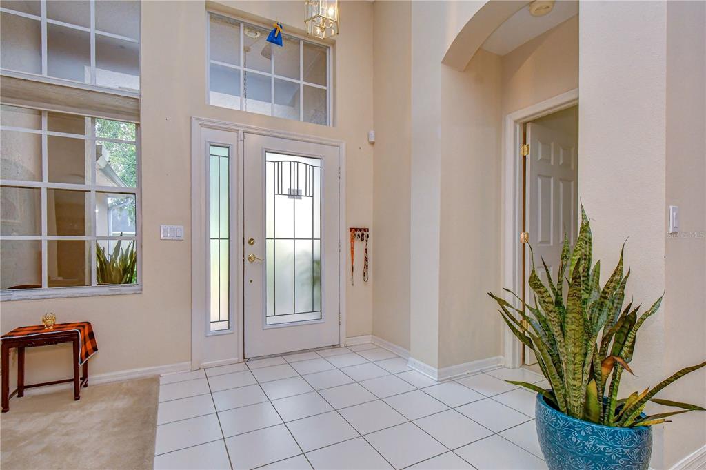 A bright entryway features white tile flooring, a glass-paneled front door, and a tall ceiling — 2202 LONGMORE CIRCLE, VALRICO, FL