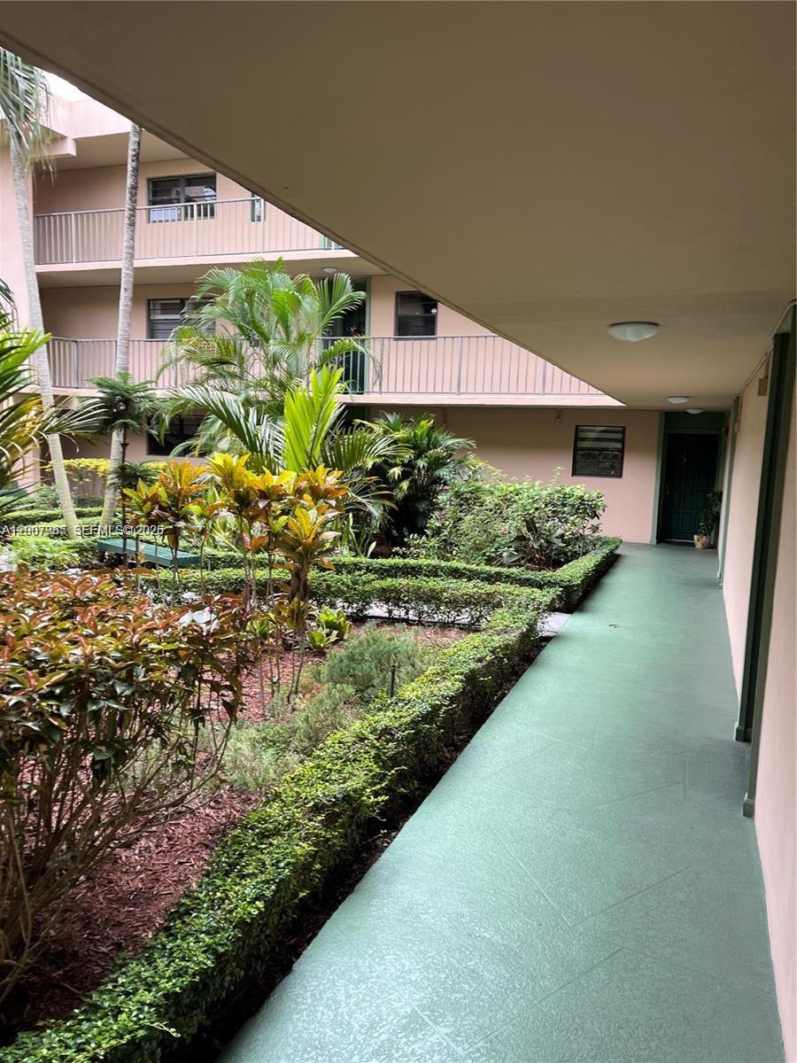 An outdoor walkway overlooks a landscaped courtyard with tropical plants and a multi-story building — 10525 SW 112th Ave # 114, Miami FL 33176, MIAMI, FL