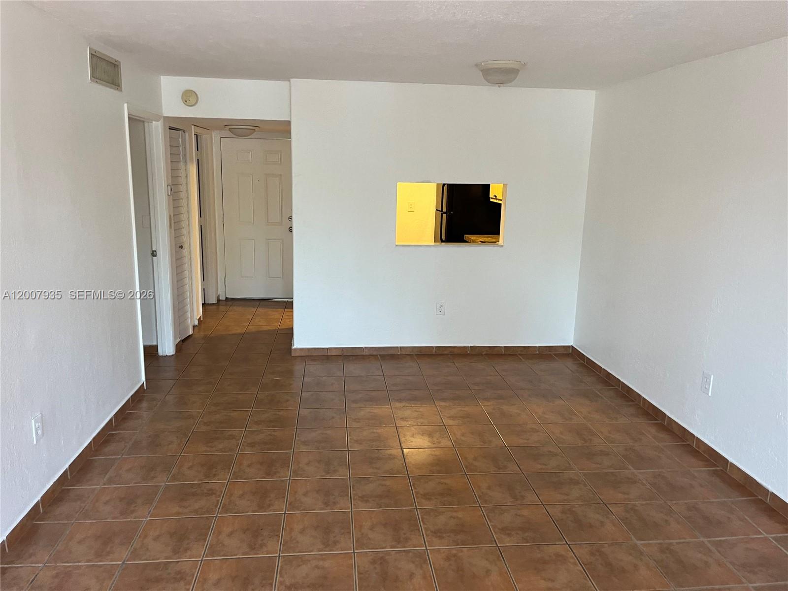 An empty room features brown tile flooring, white walls, and a rectangular kitchen pass-through window — 10525 SW 112th Ave # 114, Miami FL 33176, MIAMI, FL