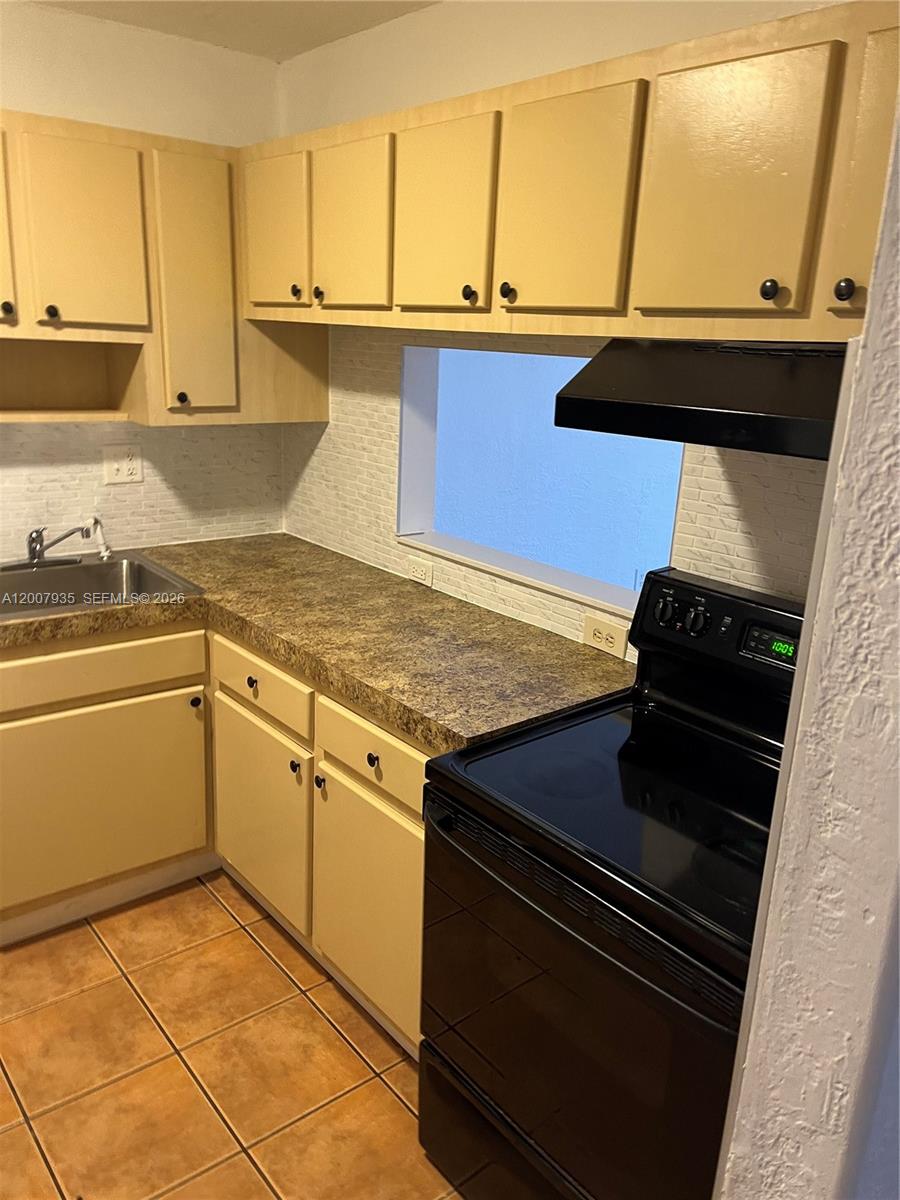 A kitchen features light-colored cabinets, a dark countertop, a black stove, and tiled flooring — 10525 SW 112th Ave # 114, Miami FL 33176, MIAMI, FL