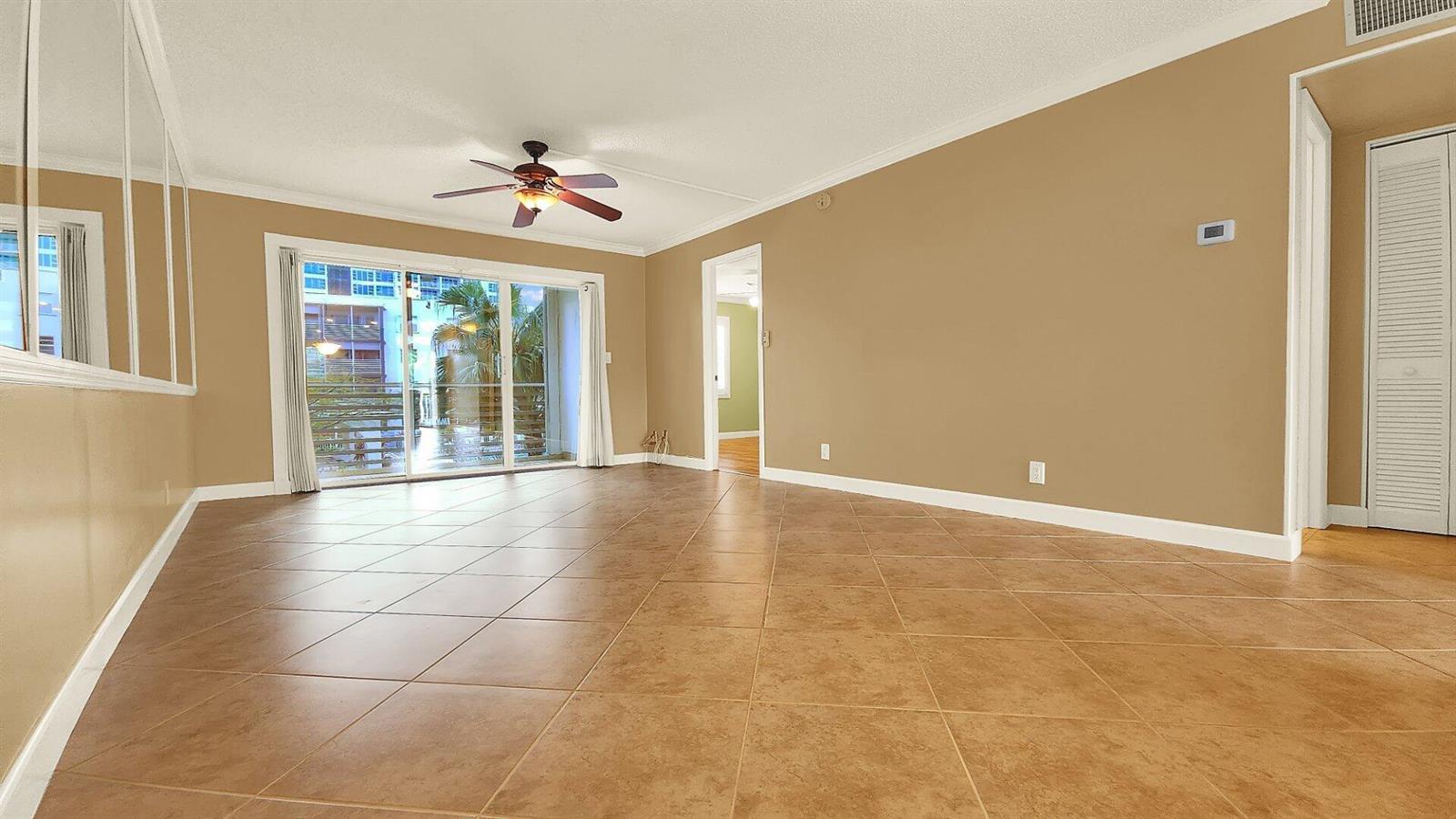 An empty living room features tan walls, large square floor tiles, and a sliding glass door — 1541 S Ocean Boulevard # 211, Pompano Beach FL 33062, POMPANO BEACH, FL