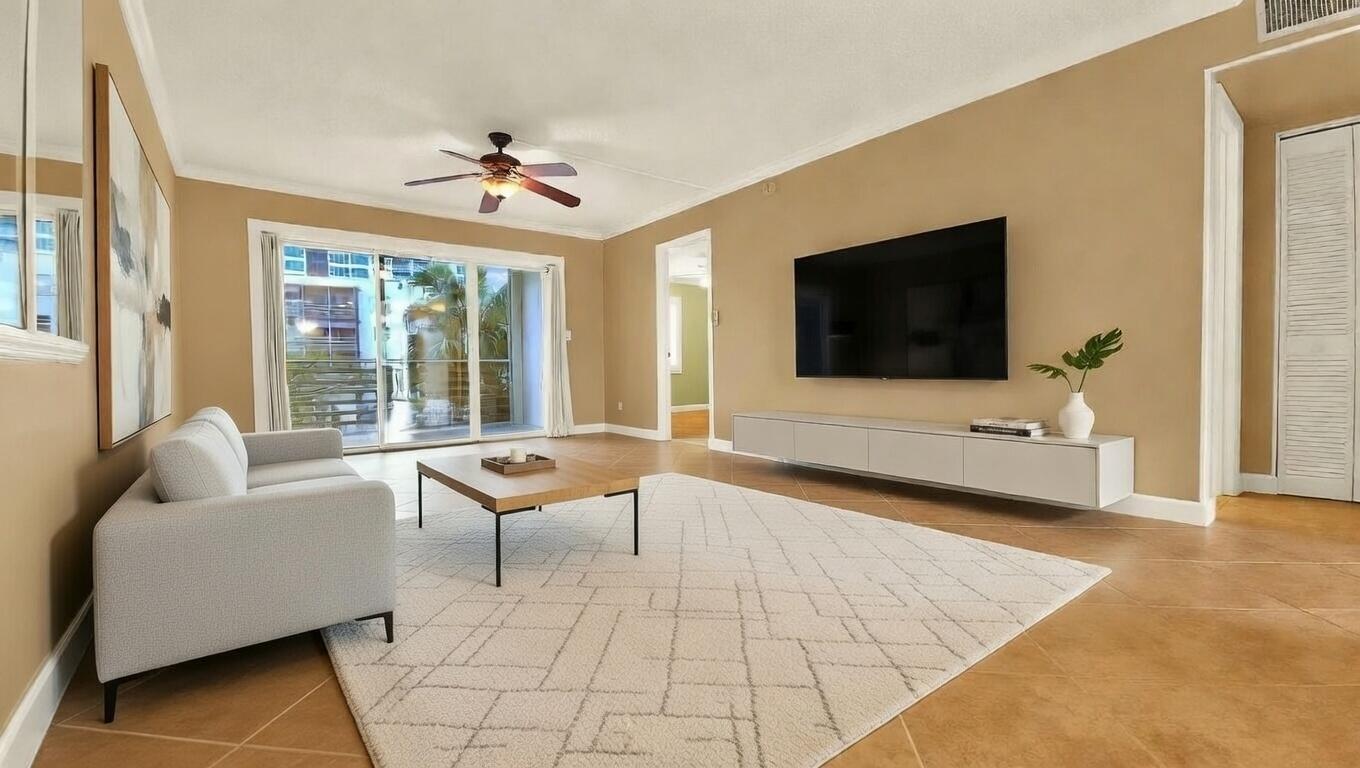 A living room with a light gray sofa, area rug, wall-mounted television, and tile flooring — 1541 S Ocean Boulevard # 211, Pompano Beach FL 33062, POMPANO BEACH, FL