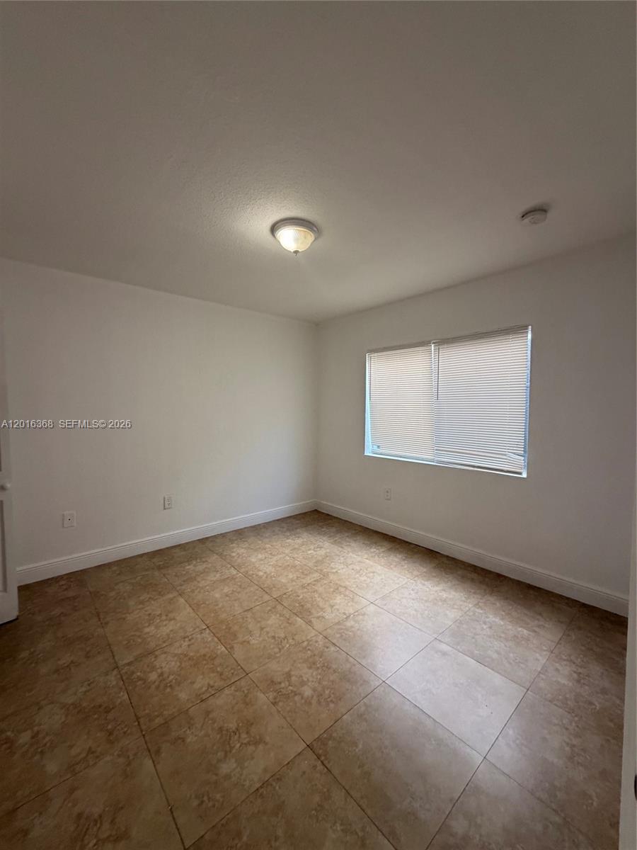 An empty room features white walls, a ceiling light, a window with blinds, and tile flooring — 219 NW 10th St # 2, Miami FL 33136, MIAMI, FL