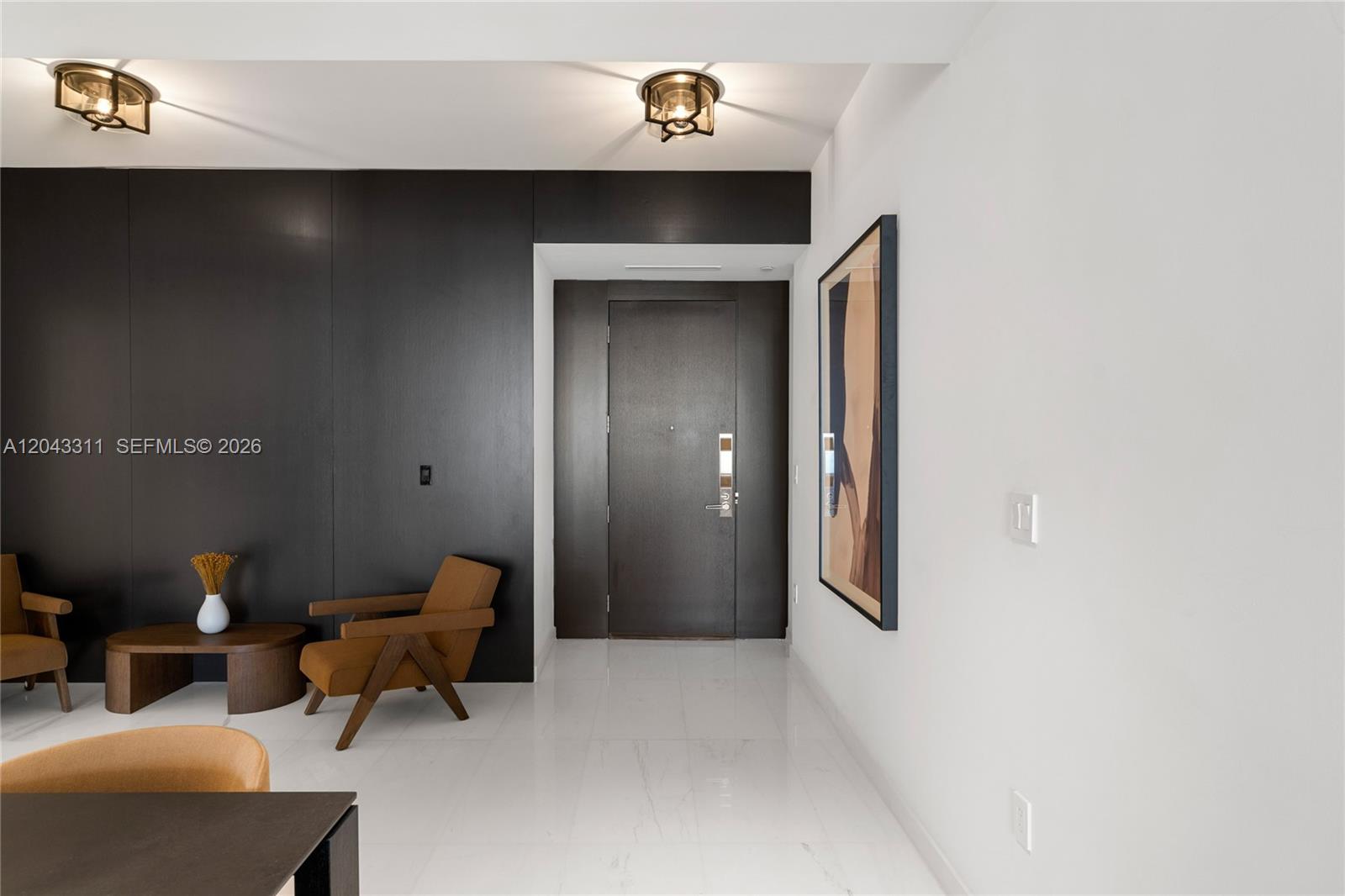 An entryway features a dark wood accent wall, a brown armchair, and white tile flooring — 300 Biscayne Boulevard Way # 4009W, Miami FL 33131, MIAMI, FL