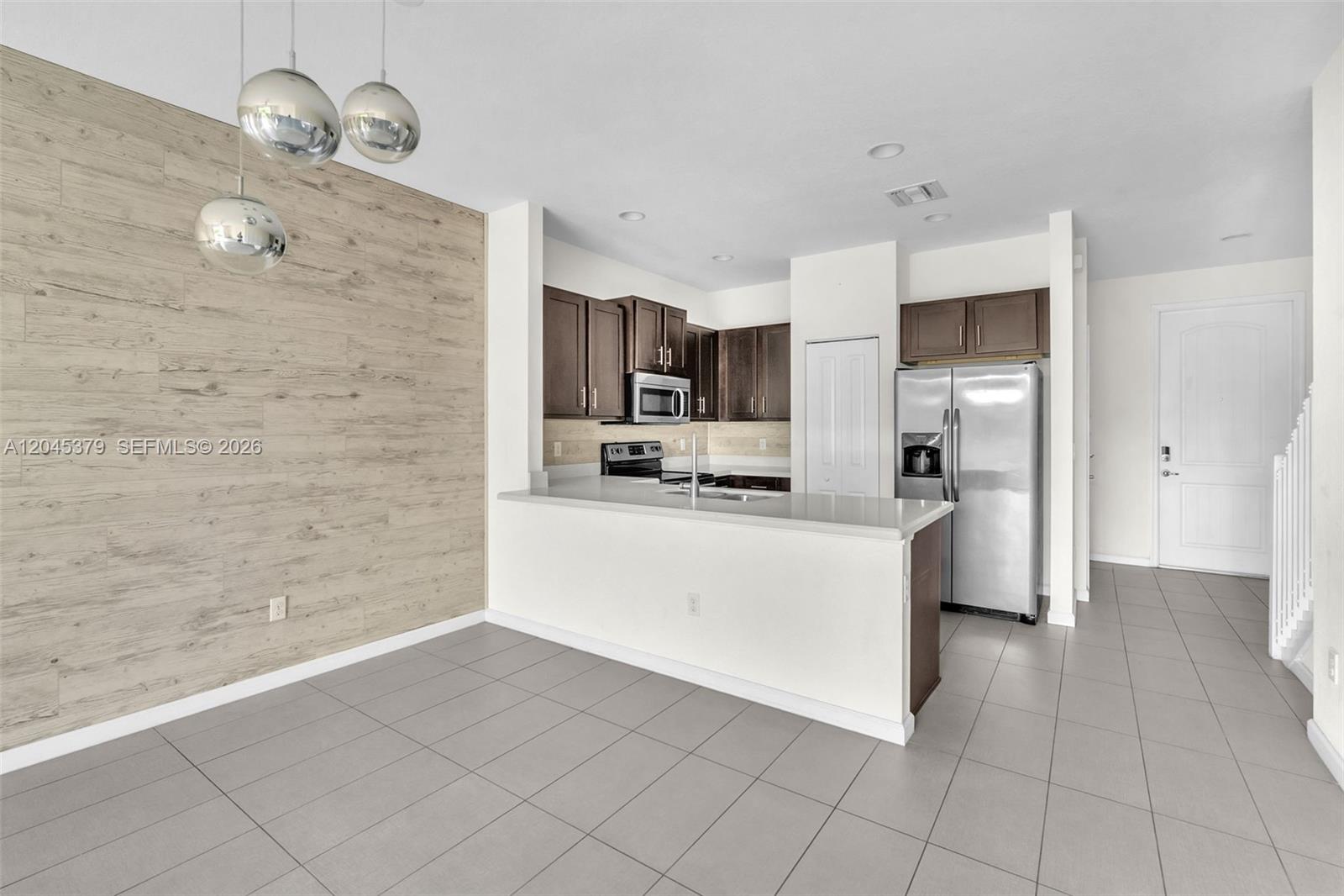 A kitchen with dark wood cabinets, stainless steel appliances, and a light wood-paneled accent wall — OAKLAND PARK, FL