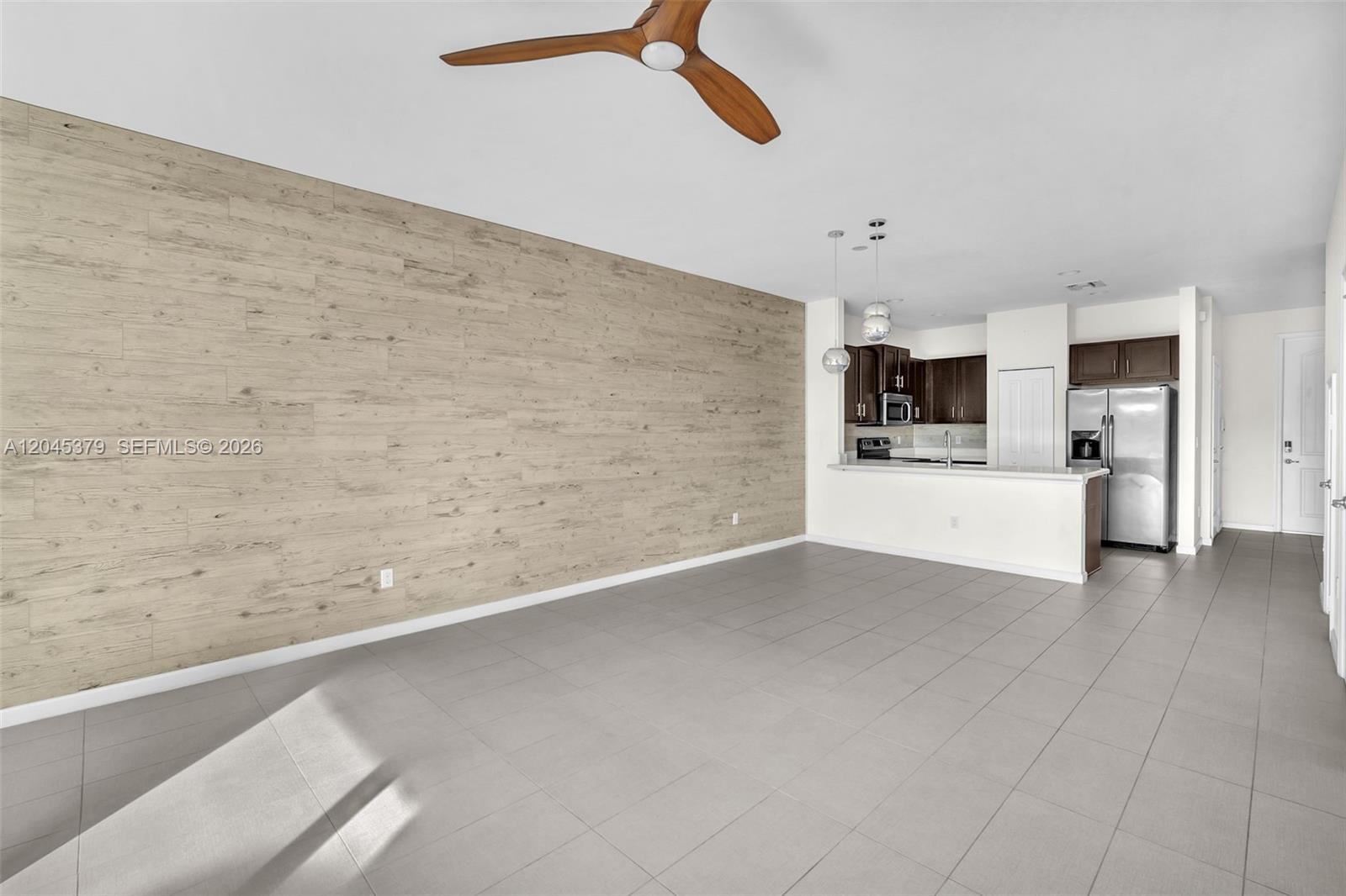 An open-concept living area features a wood-paneled accent wall, tile flooring, and an adjacent kitchen — OAKLAND PARK, FL