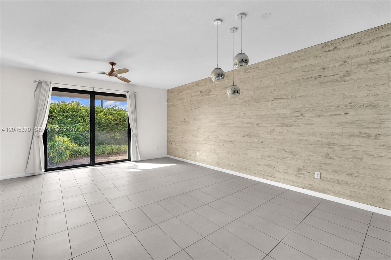 A living room features light-colored tile flooring, a wood-look accent wall, and sliding glass doors — OAKLAND PARK, FL