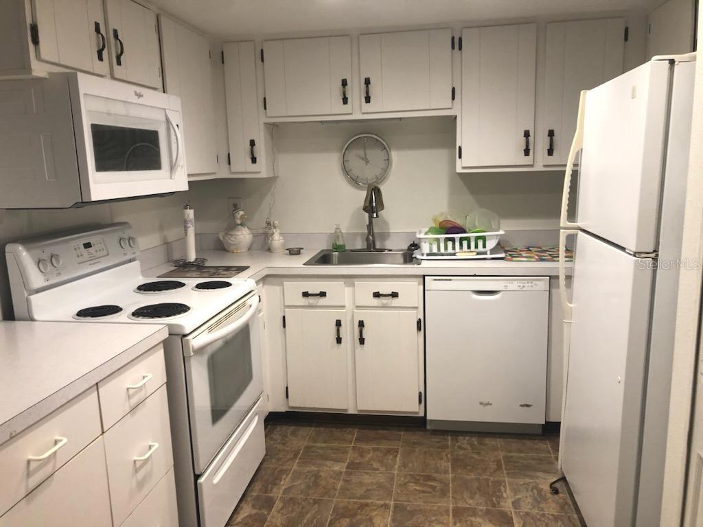 A kitchen with white cabinets, white appliances, a double sink, and brown tile flooring — 532 BAHIA CIRCLE UNIT A, OCALA, FL