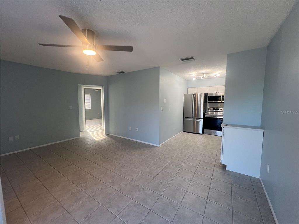 An open-concept room features light blue walls, tiled floors, a ceiling fan, and a kitchen — 810 KINGS COURT UNIT D, PUNTA GORDA, FL