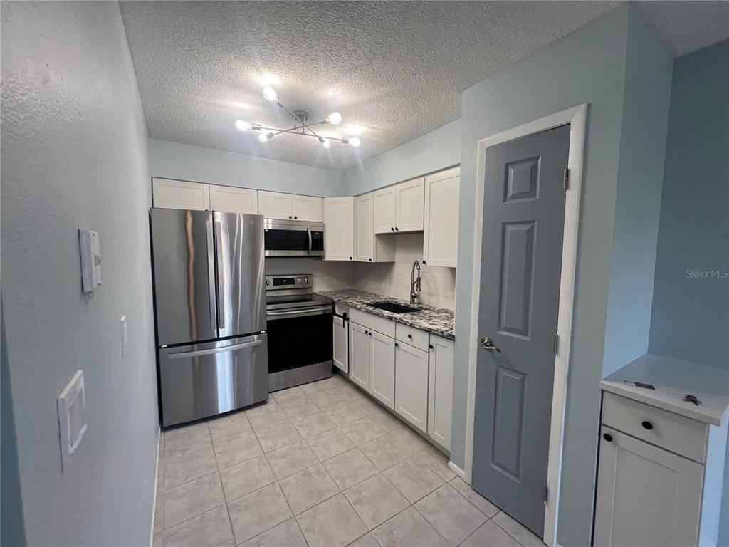 A kitchen features white cabinets, stainless steel appliances, granite countertops, and light gray tile flooring — 810 KINGS COURT UNIT D, PUNTA GORDA, FL