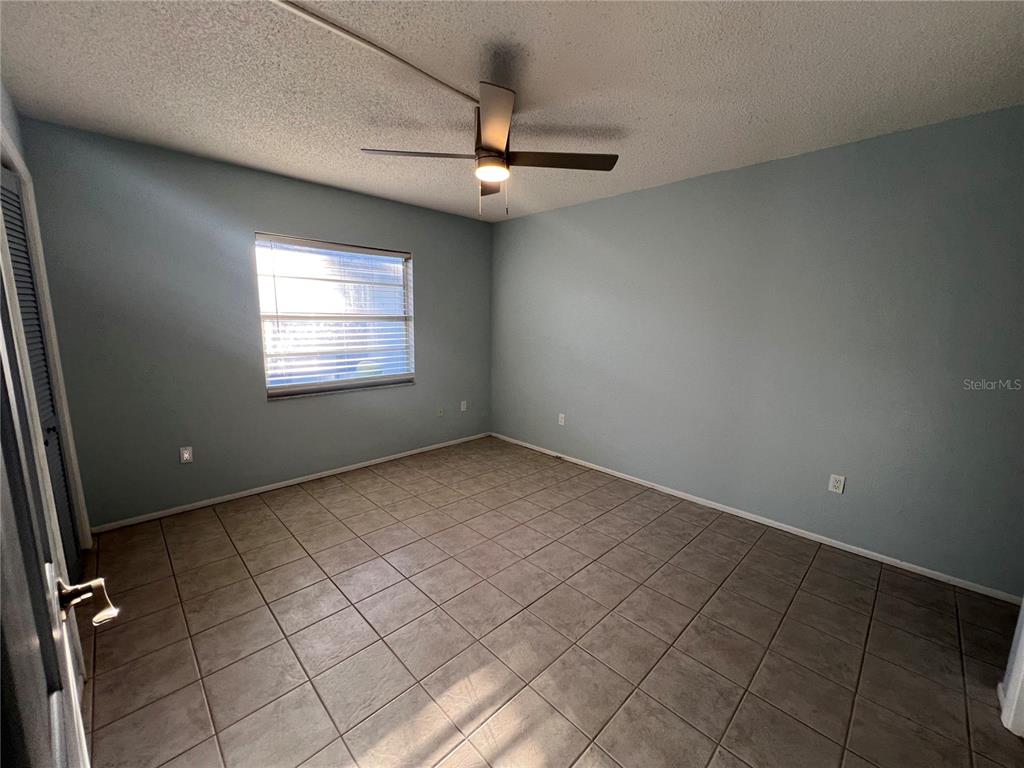 An empty bedroom features light blue walls, tile flooring, and a ceiling fan — 810 KINGS COURT UNIT D, PUNTA GORDA, FL