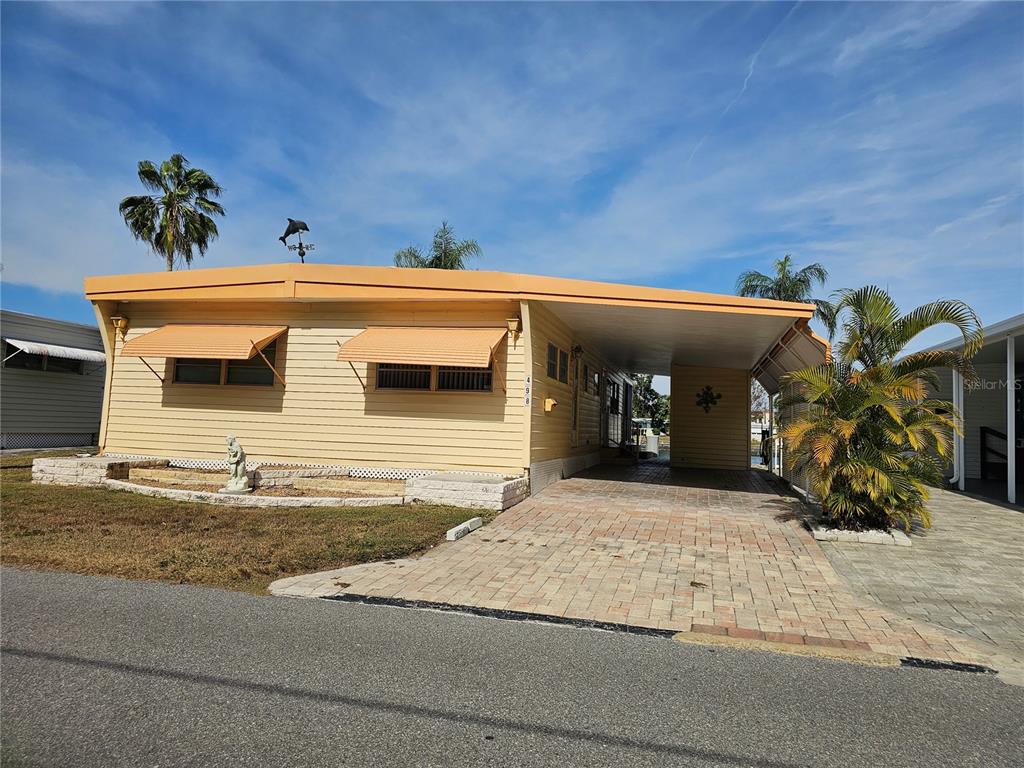A yellow mobile home features a paved carport, window awnings, and a small front garden — 18675 US HIGHWAY 19 N UNIT 498, CLEARWATER, FL