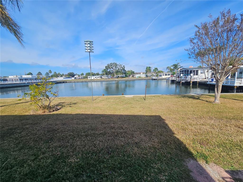 A grassy lawn overlooks a calm canal with boat docks and residential buildings in the distance — 18675 US HIGHWAY 19 N UNIT 498, CLEARWATER, FL