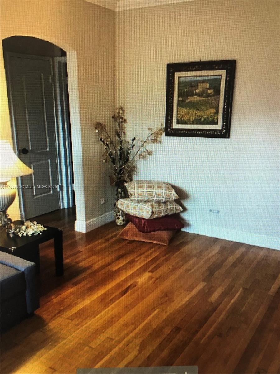A living room features hardwood floors, a framed landscape painting, and a stack of floor cushions — 30 Almeria Ave # 6, Coral Gables FL 33134, CORAL GABLES, FL