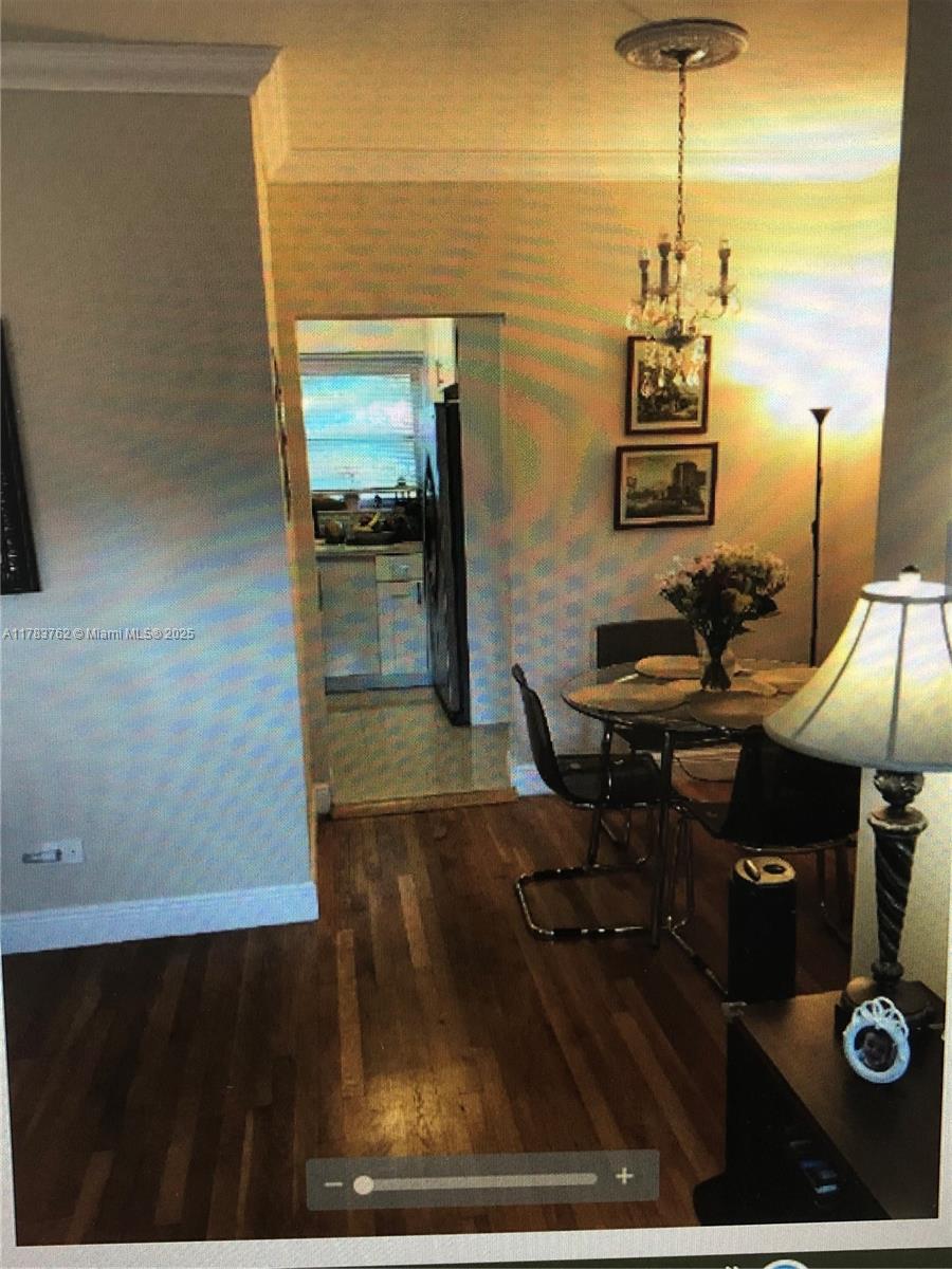A dining area with a glass table, chandelier, and hardwood floors leads into a kitchen — 30 Almeria Ave # 6, Coral Gables FL 33134, CORAL GABLES, FL