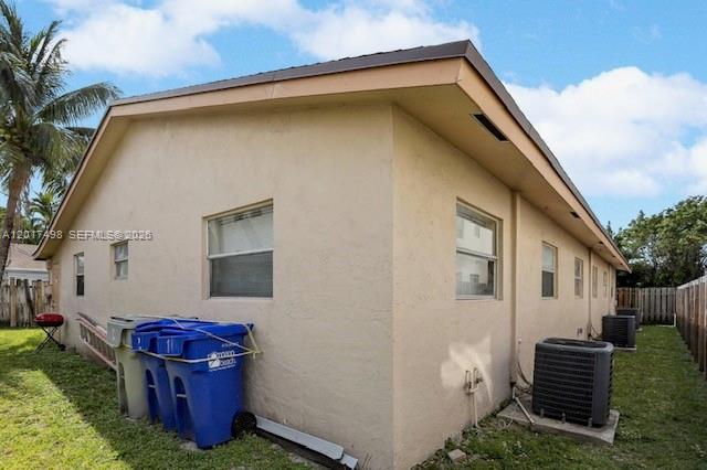 The exterior of a tan, single-story house features blue trash bins and air conditioning units — 231 SW 8th Ct, Pompano Beach FL 33060, POMPANO BEACH, FL