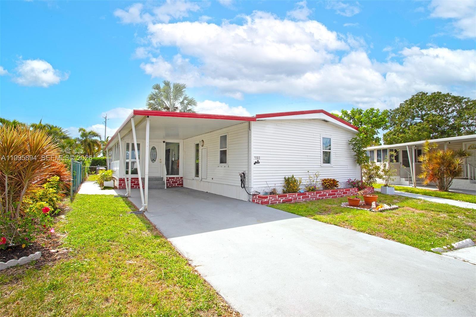 A white mobile home features a red roof, a carport, and a small brick planter — 5103 NW 1st Way, Deerfield Beach FL 33064, DEERFIELD BEACH, FL