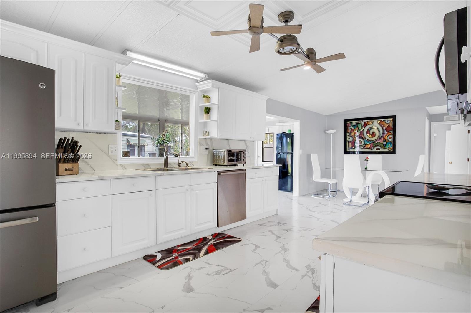 A white kitchen features marble-patterned floors, stainless steel appliances, and a dining area — 5103 NW 1st Way, Deerfield Beach FL 33064, DEERFIELD BEACH, FL