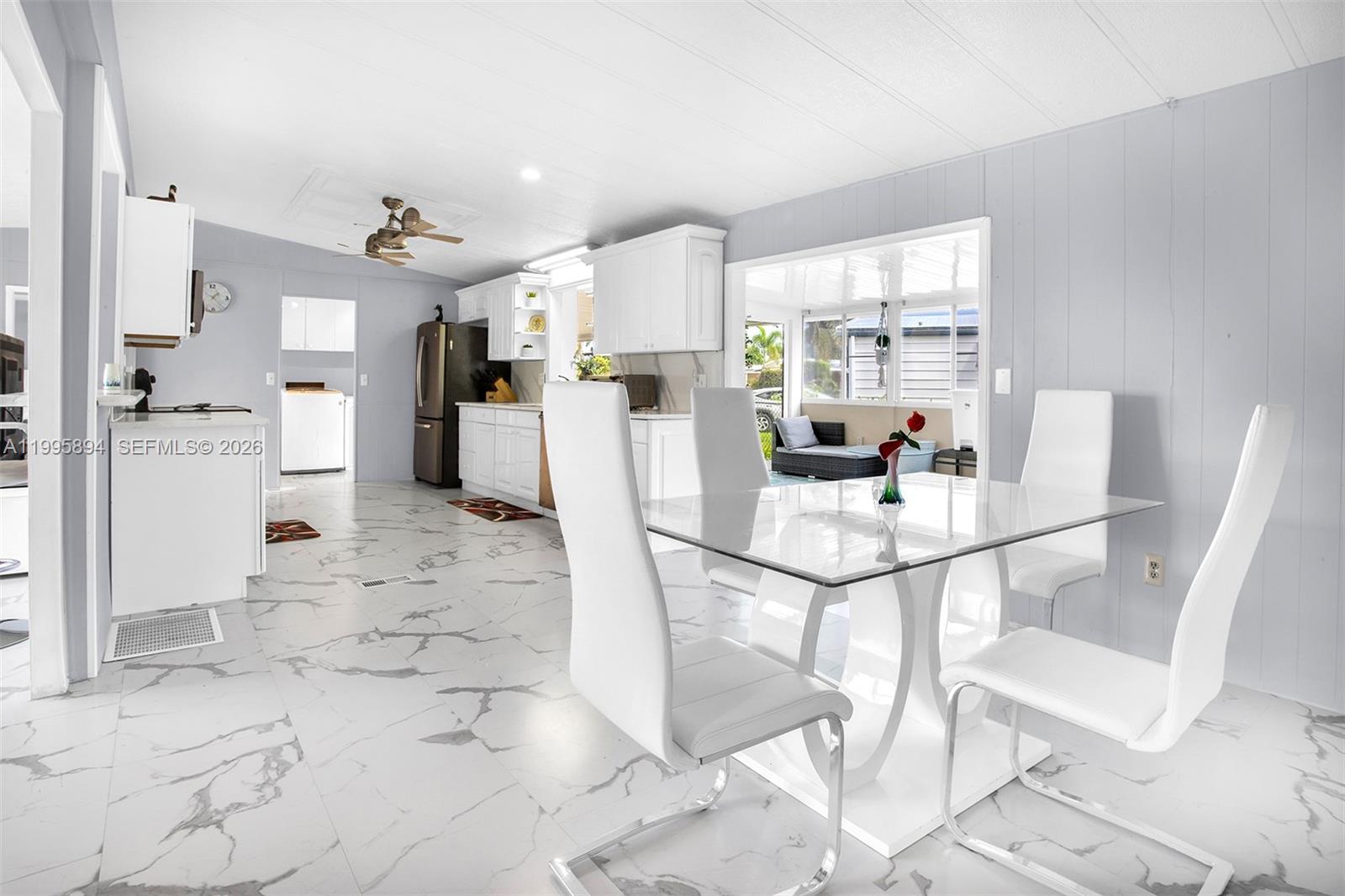 A dining area with a glass table and white chairs opens into a white kitchen — 5103 NW 1st Way, Deerfield Beach FL 33064, DEERFIELD BEACH, FL