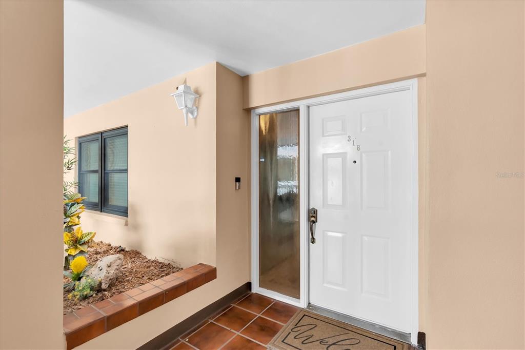 A white front door with a side window sits on a tiled porch — 6500 SUNSET WAY UNIT 316, ST PETE BEACH, FL