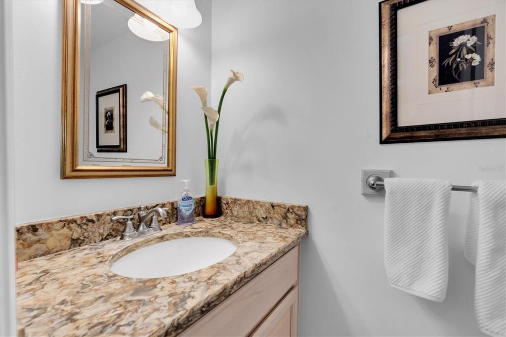 A bathroom features a granite vanity countertop, a framed mirror, and a wall-mounted towel rack — 6500 SUNSET WAY UNIT 316, ST PETE BEACH, FL