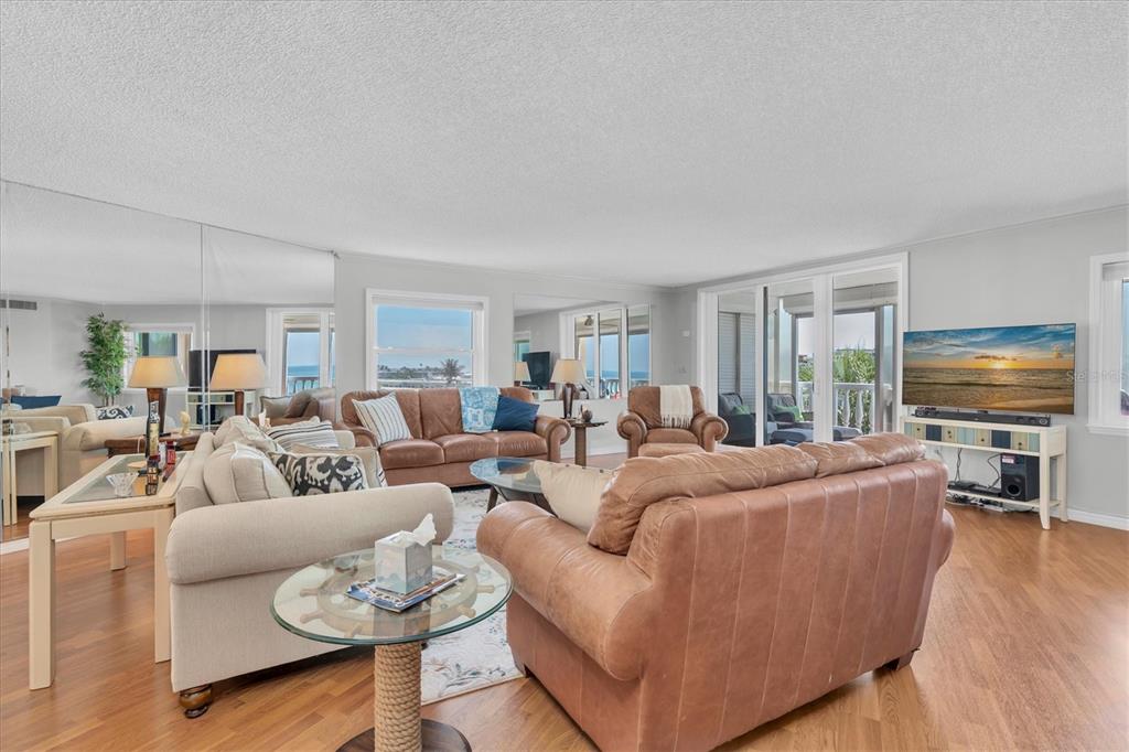 A living room features leather and fabric sofas, hardwood floors, and a large wall mirror — 6500 SUNSET WAY UNIT 316, ST PETE BEACH, FL