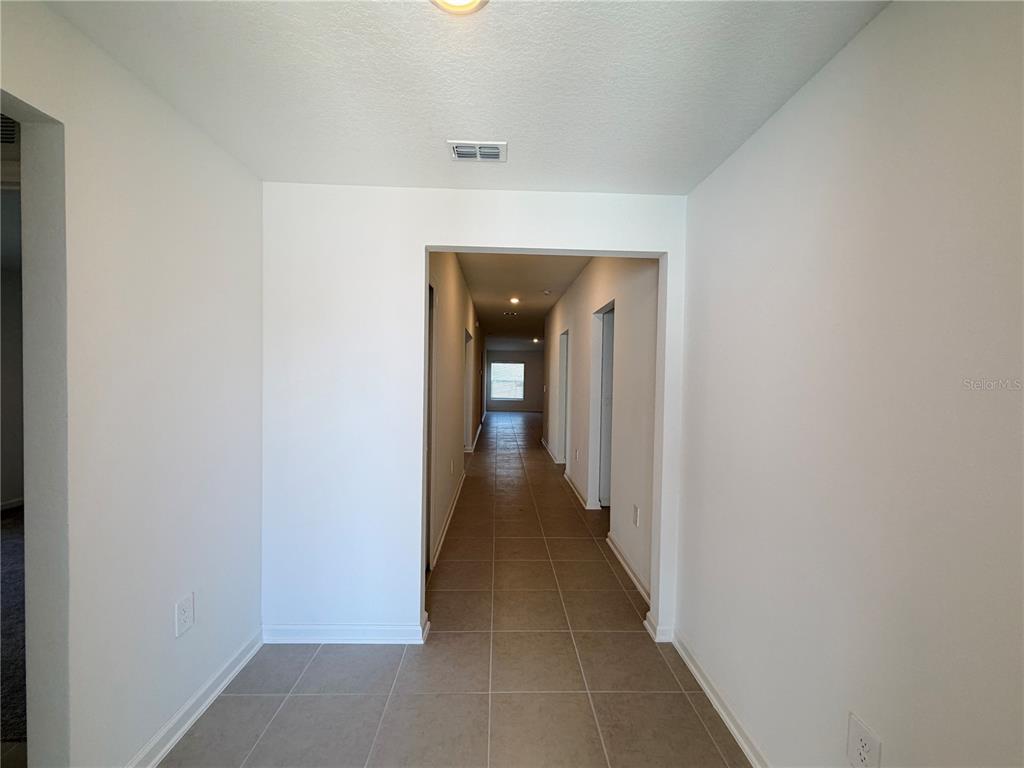 A view down a tiled hallway with white walls leading to a windowed room — 3111 TOTEM ROAD, EAGLE LAKE, FL
