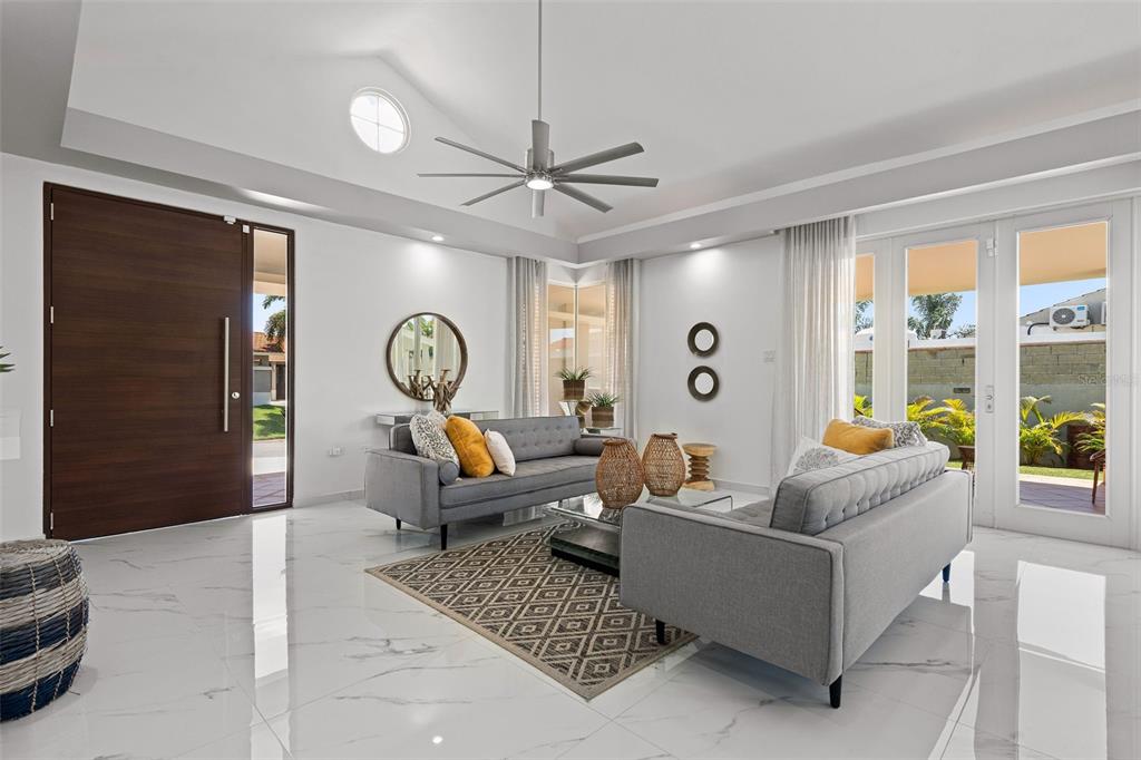 A modern living room features white marble floors, two gray sofas, and a large front door — 170 CAMINO DE LOS JAZMINES, DORADO, PR