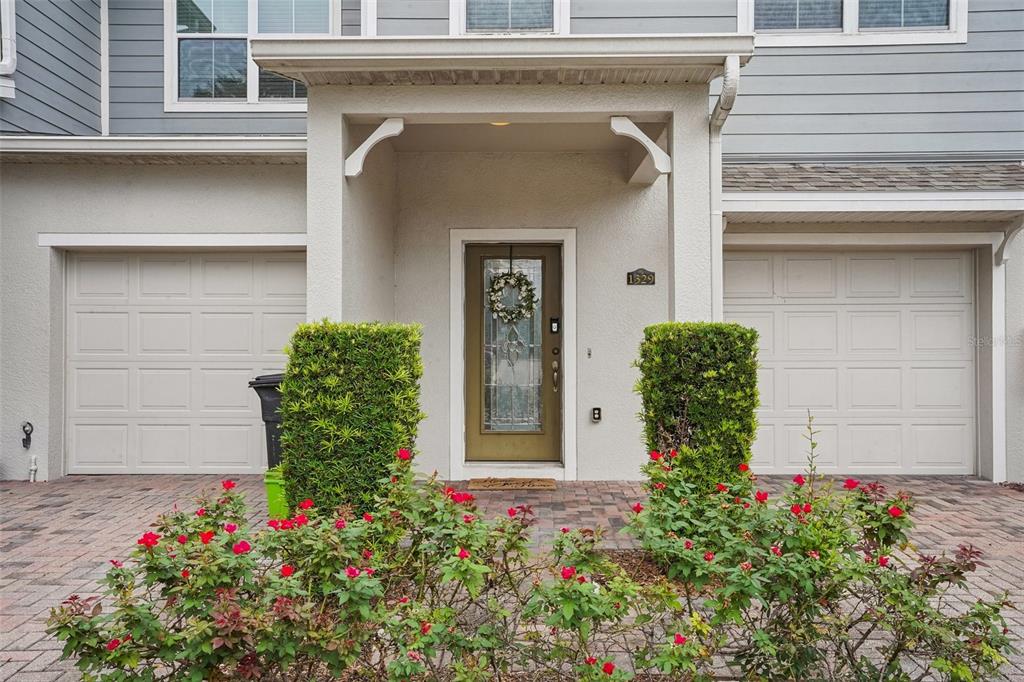 The exterior of a townhouse features a covered entryway, two garage doors, and landscaped bushes — 1329 HERITAGE COMMONS DRIVE, WINTER SPRINGS, FL