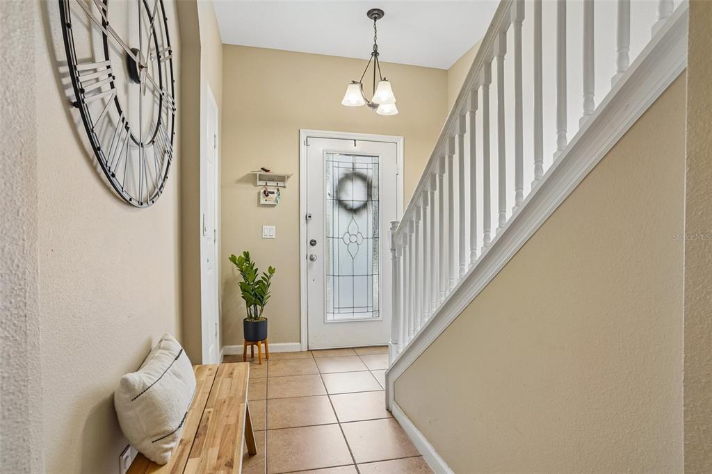 An entryway features a wooden bench, a large wall clock, tile flooring, and a staircase — 1329 HERITAGE COMMONS DRIVE, WINTER SPRINGS, FL