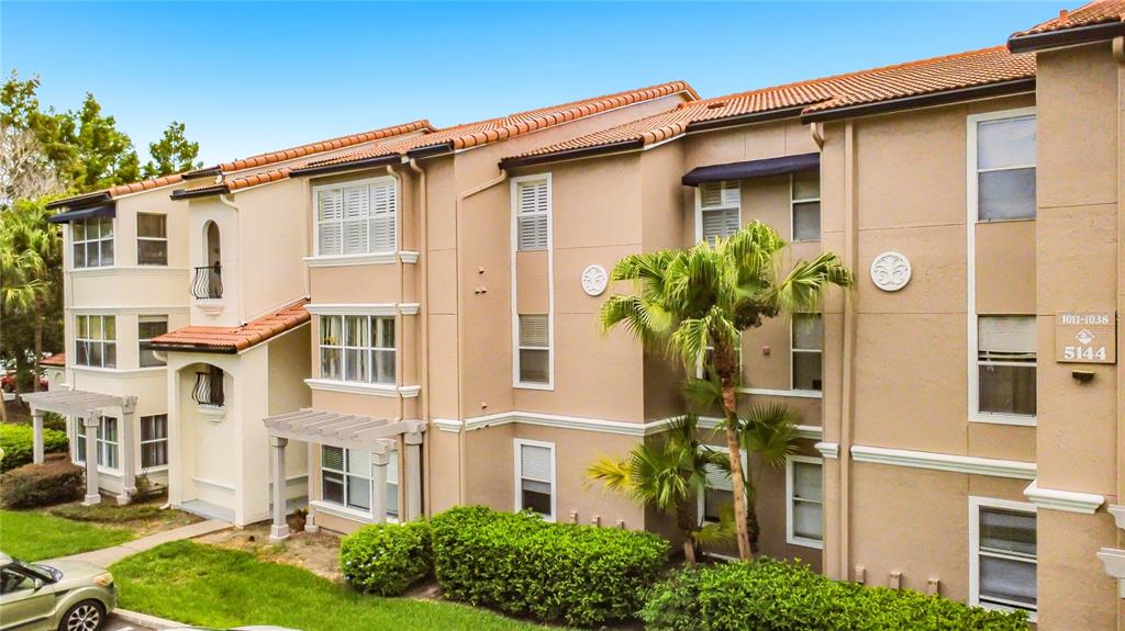 A multi-story apartment building with tan stucco walls, a tiled roof, and landscaped bushes — 5144 CONROY ROAD UNIT 13, ORLANDO, FL
