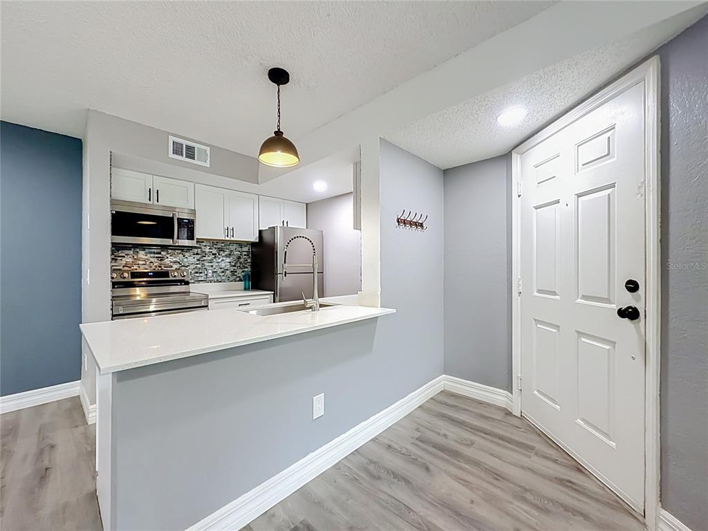 A kitchen with white cabinets, stainless steel appliances, and a breakfast bar faces an entryway — 5144 CONROY ROAD UNIT 13, ORLANDO, FL