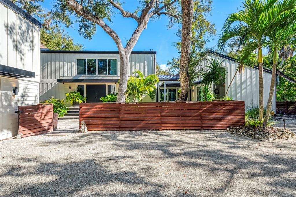 A modern two-story house with light siding, a wooden fence, and palm trees in front — 5303 HIDDEN HARBOR ROAD, SARASOTA, FL