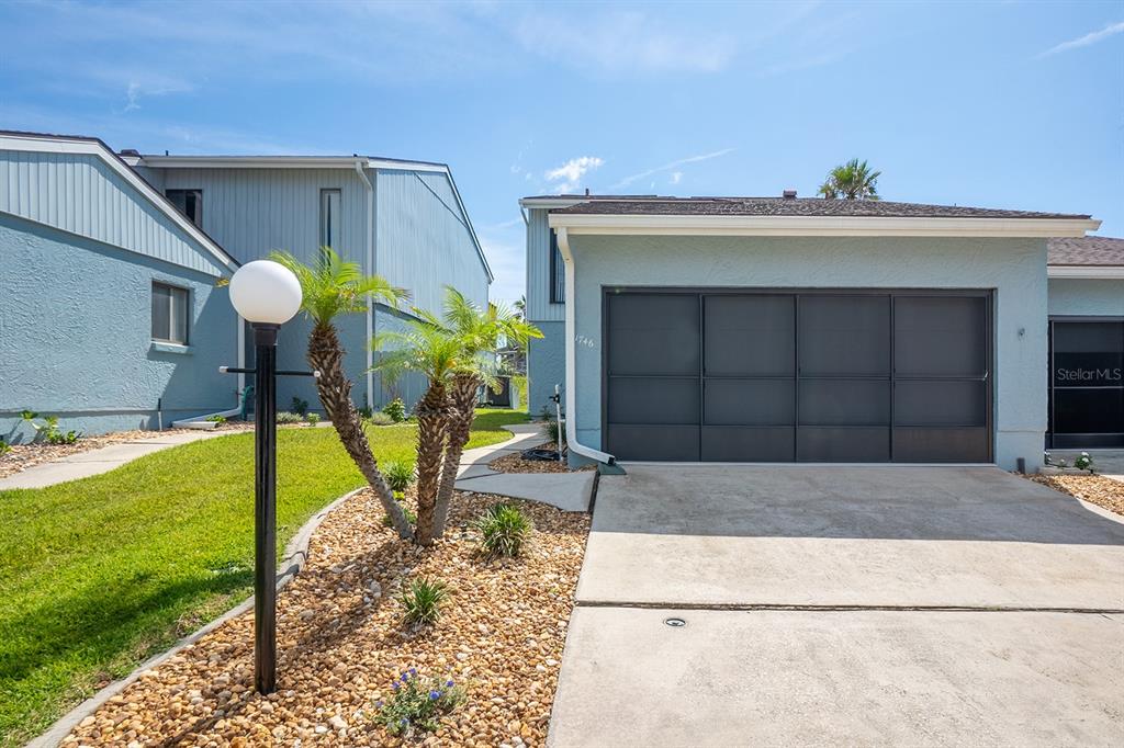 A light blue house exterior features a dark garage door, a concrete driveway, and landscaping — 1746 WINDSONG CIRCLE, FLAGLER BEACH, FL