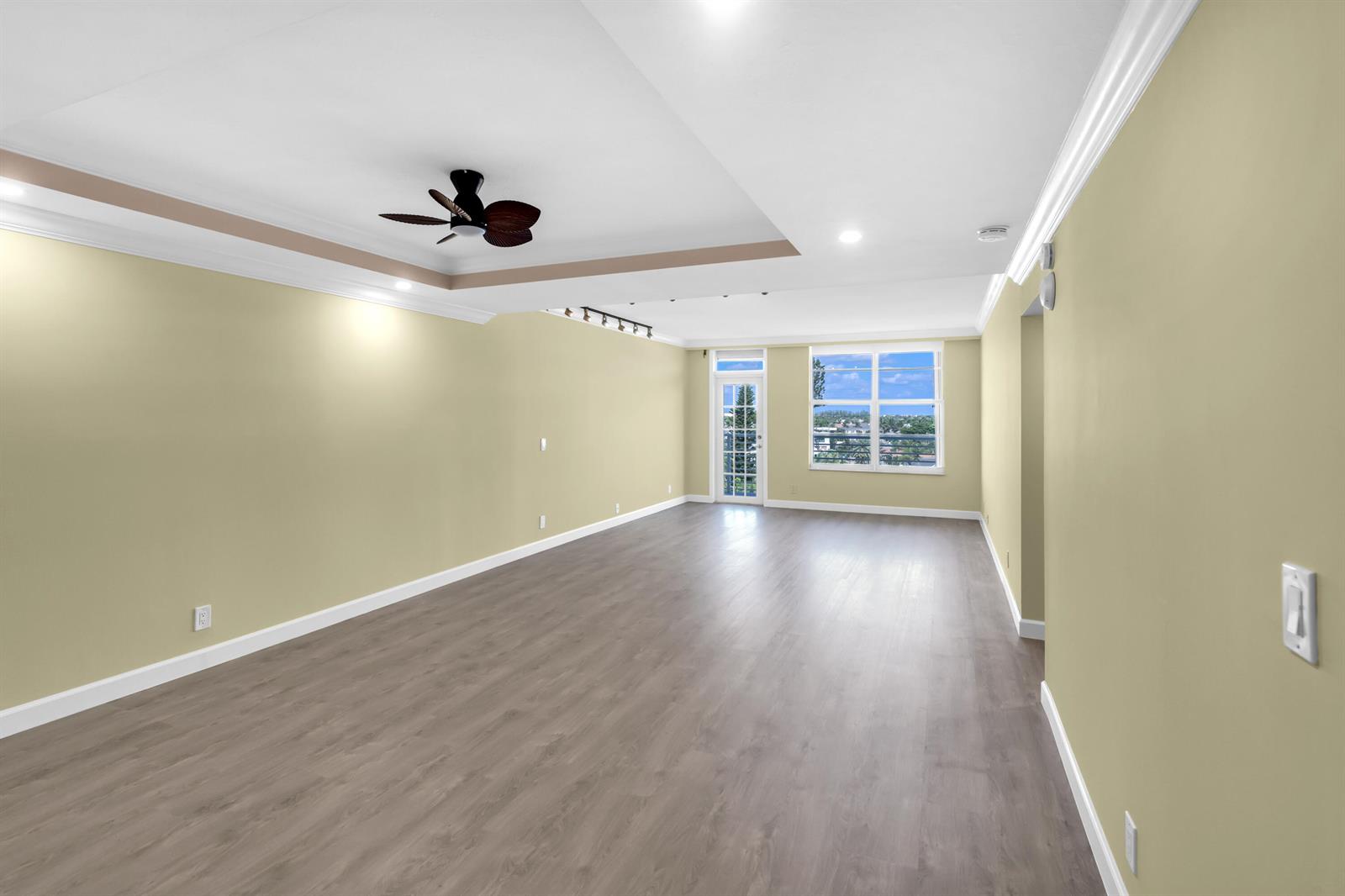 An empty living room features light green walls, wood-look flooring, a tray ceiling, and balcony access — 2851 S OCEAN Boulevard # 0086, Boca Raton FL 33432, BOCA RATON, FL