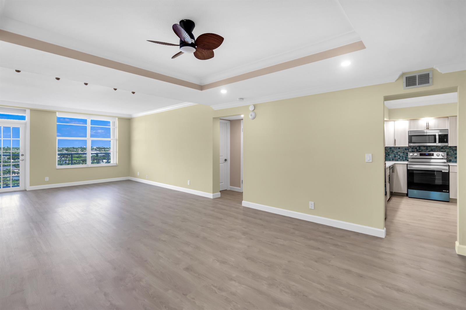 An empty living room with light wood flooring, a tray ceiling, and an adjacent kitchen — 2851 S OCEAN Boulevard # 0086, Boca Raton FL 33432, BOCA RATON, FL