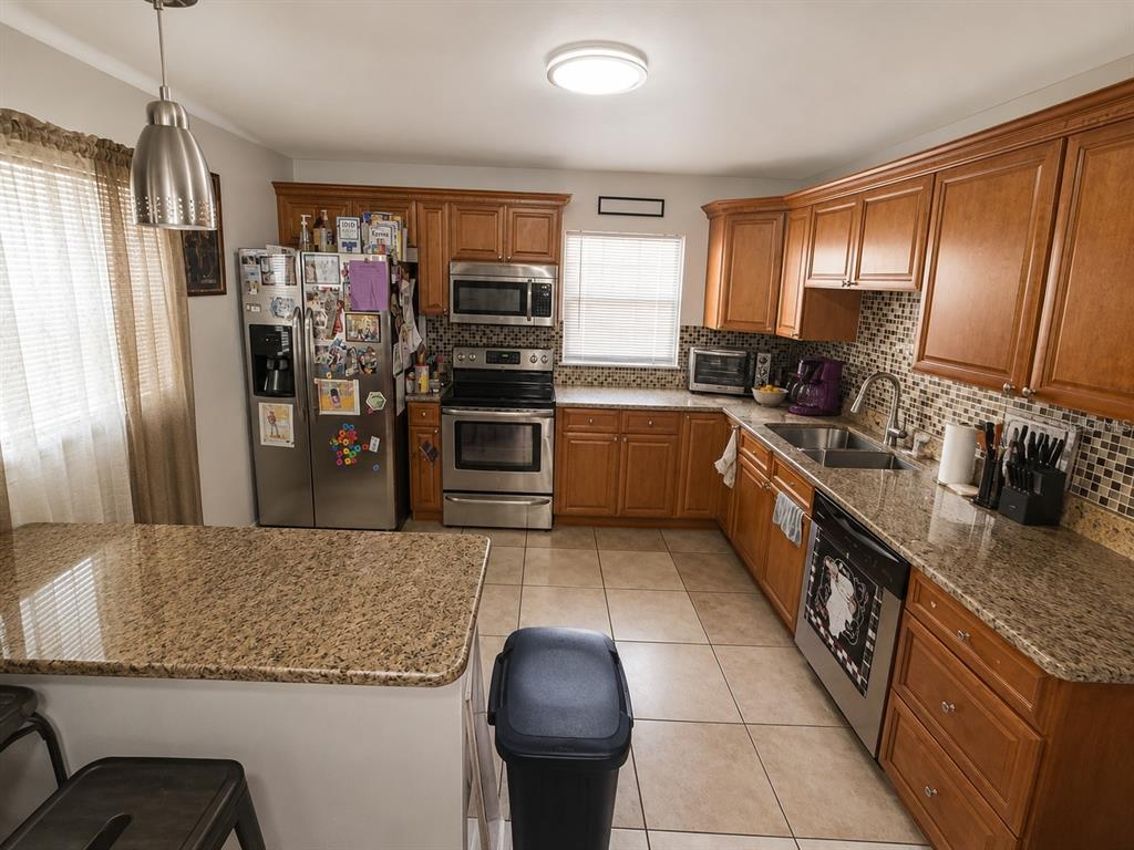 A kitchen with wood cabinets, granite countertops, stainless steel appliances, and tile flooring — 7507 W CARACAS STREET, TAMPA, FL