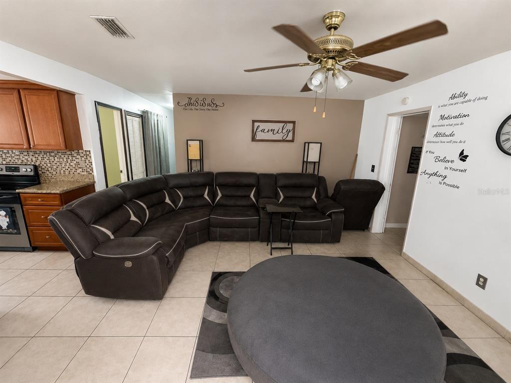 A living room features a large dark sectional sofa, a round ottoman, and a ceiling fan — 7507 W CARACAS STREET, TAMPA, FL