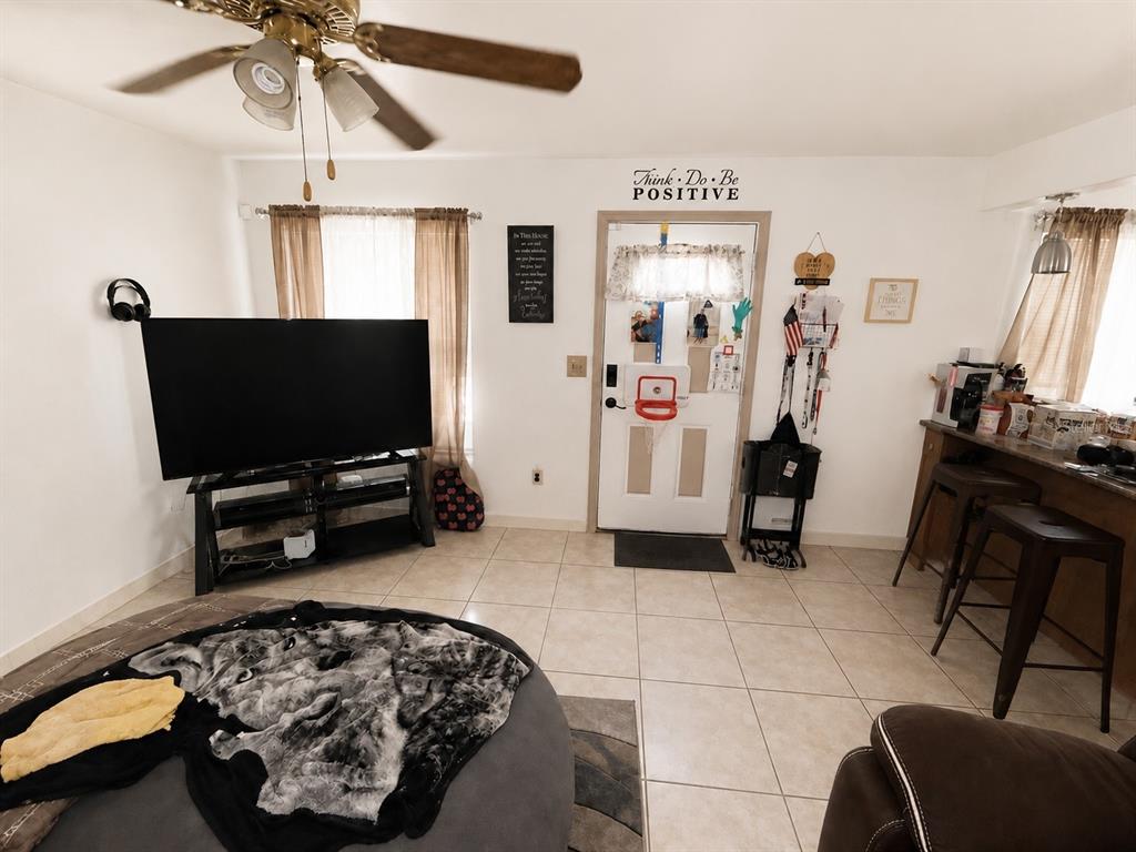 A living room with tile flooring, a large television, a ceiling fan, and an entryway door — 7507 W CARACAS STREET, TAMPA, FL