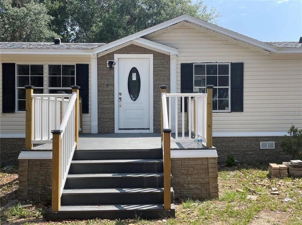 A front view of a house with beige siding, a stone facade, and a wooden deck — 30349 ELAM ROAD, WESLEY CHAPEL, FL