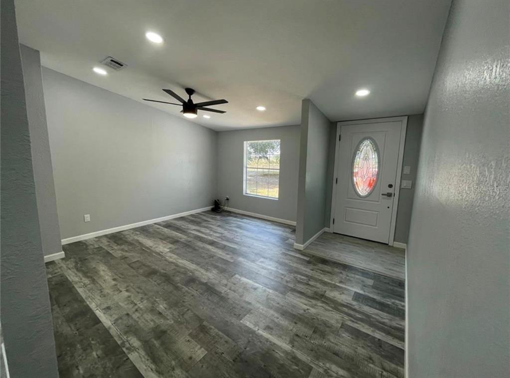 An empty room with gray walls, wood-look flooring, a ceiling fan, and a front door — 30349 ELAM ROAD, WESLEY CHAPEL, FL
