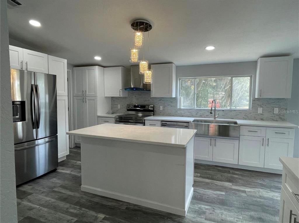 A modern kitchen features white cabinets, a central island, stainless steel appliances, and wood-look flooring — 30349 ELAM ROAD, WESLEY CHAPEL, FL