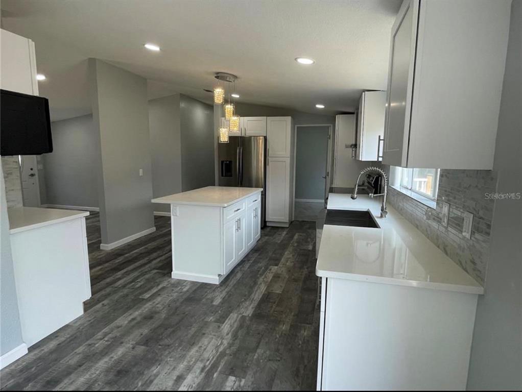A modern kitchen features white cabinets, a central island, and gray wood-look flooring — 30349 ELAM ROAD, WESLEY CHAPEL, FL
