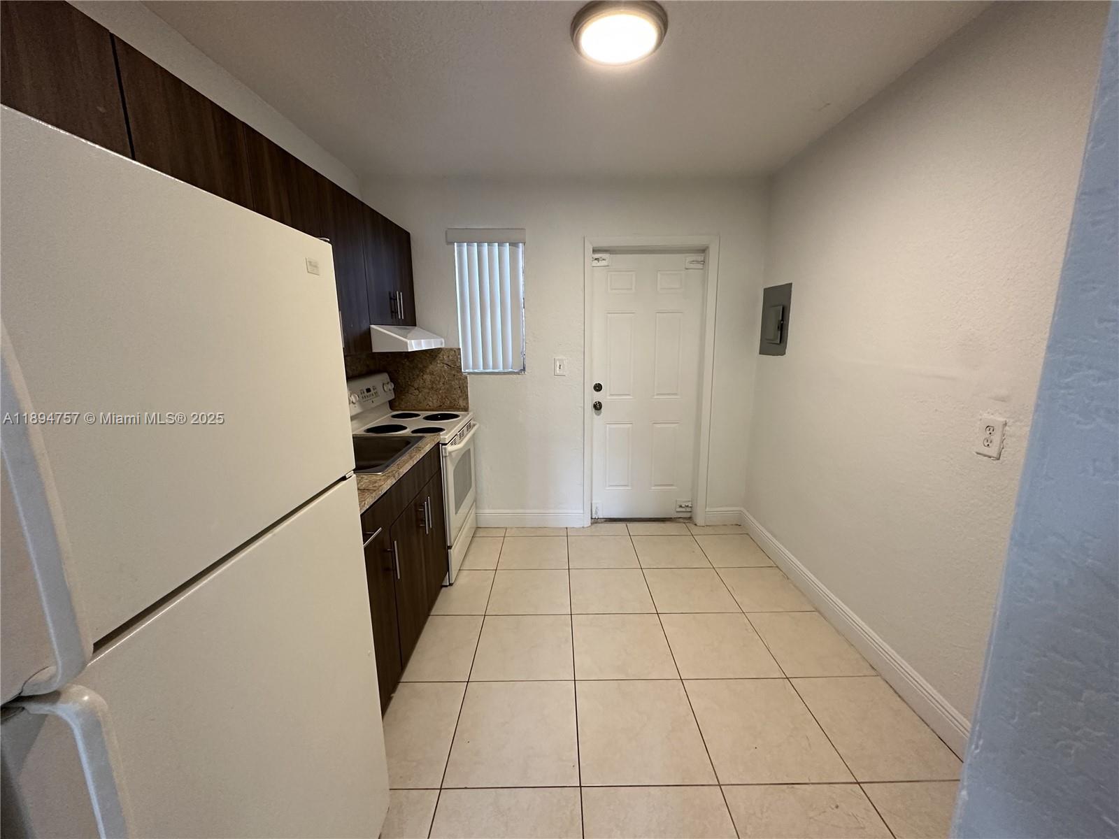 A small kitchen features dark wood cabinets, white appliances, and light-colored floor tiles — 1851 Ali Baba Ave # 4, Opa-Locka FL 33054, OPA-LOCKA, FL
