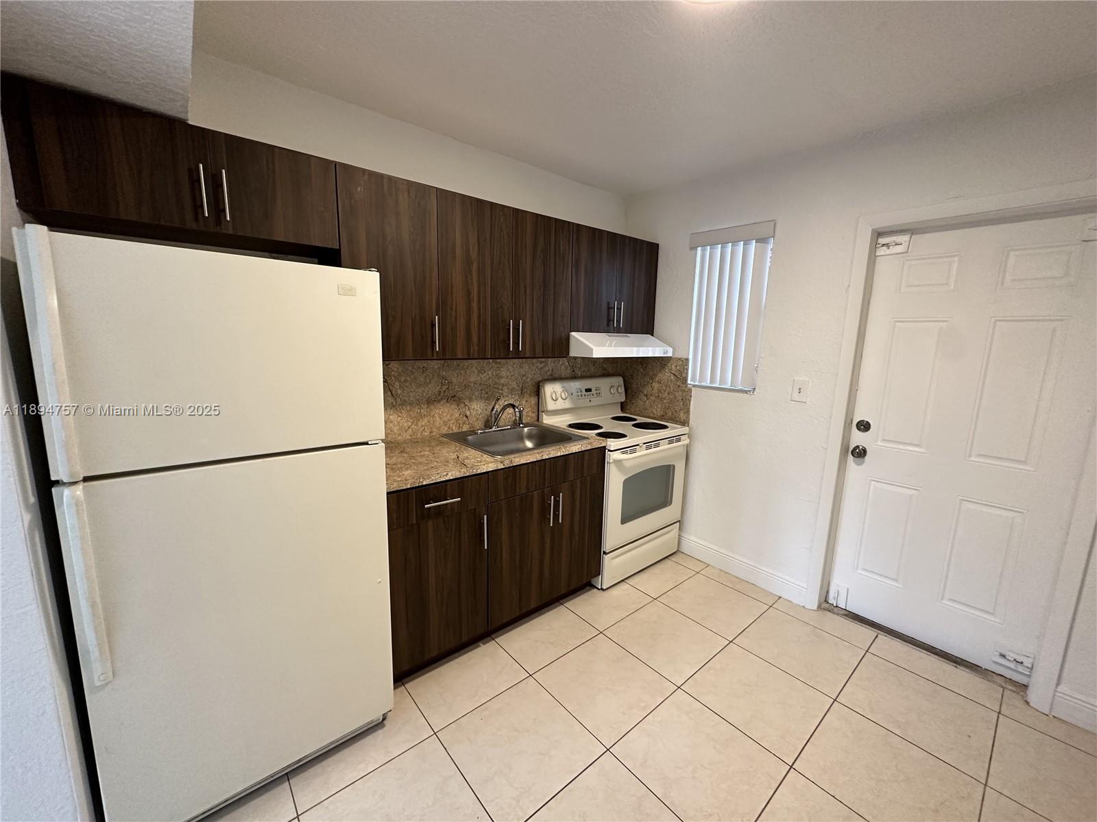 A kitchen features dark wood cabinets, white appliances, a stone countertop, and light tile flooring — 1851 Ali Baba Ave # 4, Opa-Locka FL 33054, OPA-LOCKA, FL