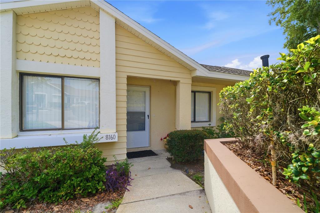 A yellow house exterior features a concrete walkway leading to a white front door — 8160 STURBRIDGE COURT UNIT 8160, WEEKI WACHEE, FL